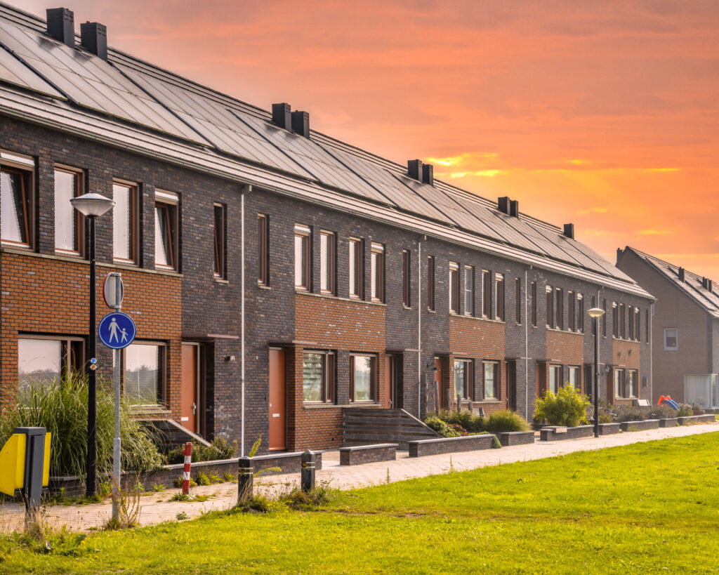 Row of modern family houses in contemporary street. New ecological neighborhood with solar panels under orange sky. Small gardens. Street view in Heerhugowaard, Netherlands.